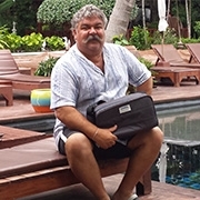 Mann sitzt im Urlaub auf einer Liege beim Pool und lächelt mit DreamStation Reisetasche in der Hand in die Kamera